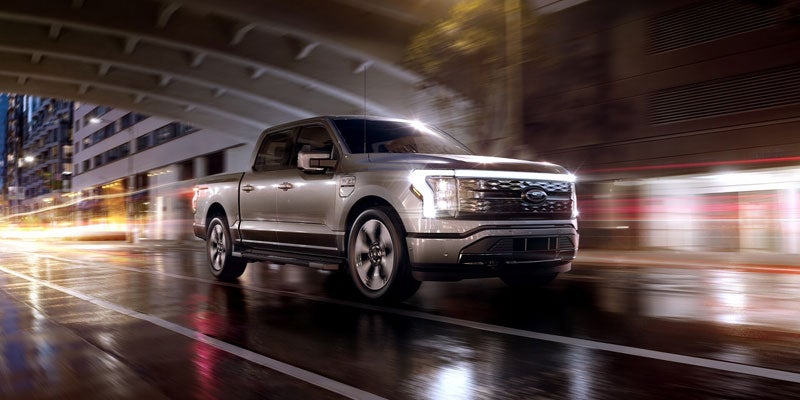 Silver Ford F-150 Lightning driving under a city bridge
